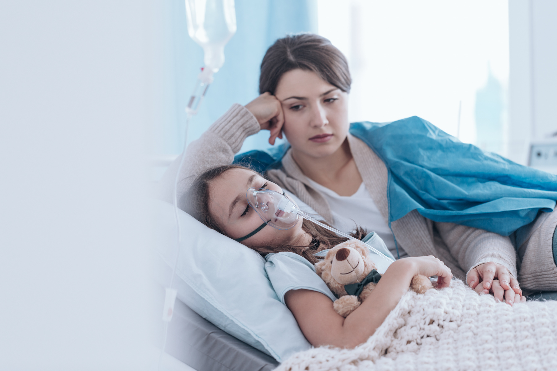 Child lying in the hospital in an oxygen mask and her mother looking at her